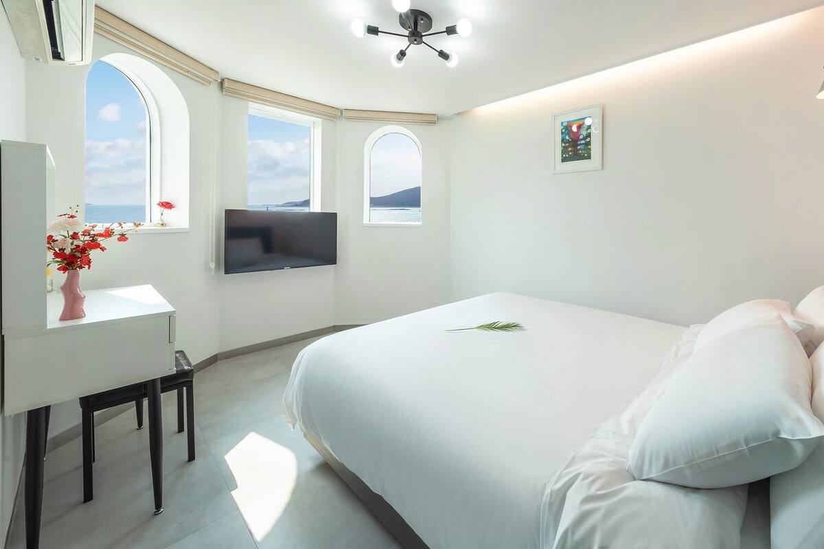 Ein Schlafzimmer mit Bett, Schreibtisch, Wandfernseher und Meerblick aus dem Fenster.