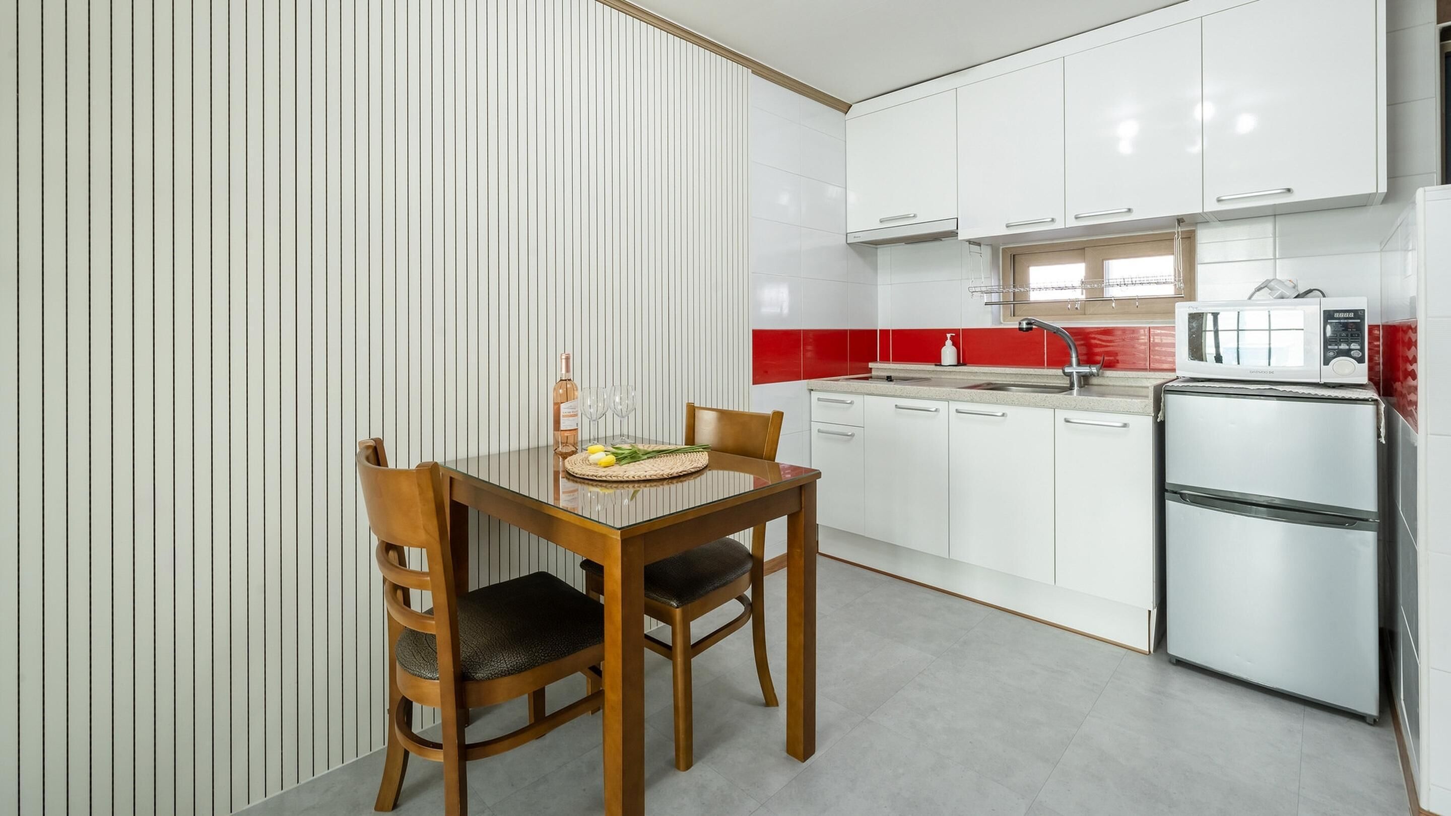 Una cocina compacta con muebles blancos, un refrigerador de acero inoxidable y una mesa de comedor con sillas.