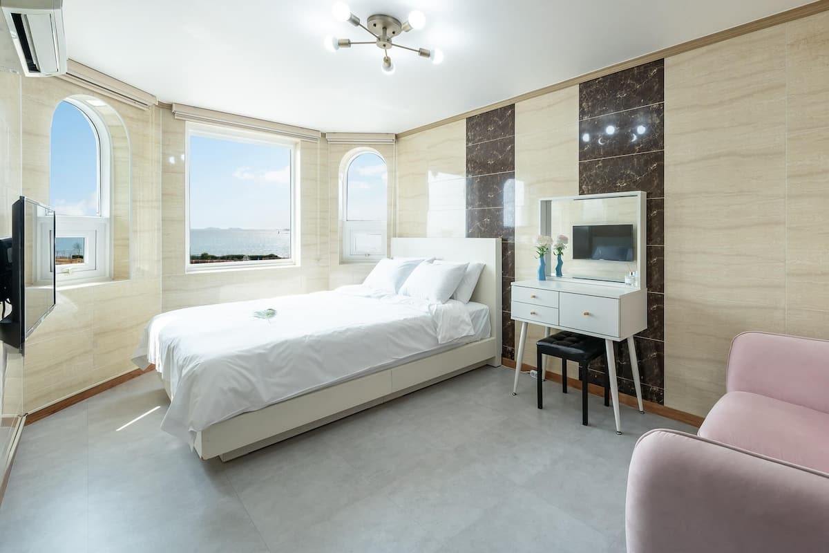 Ein modernes Schlafzimmer mit einem Bett, einem Schreibtisch, einem Stuhl und einem rosa Schlafsofa.