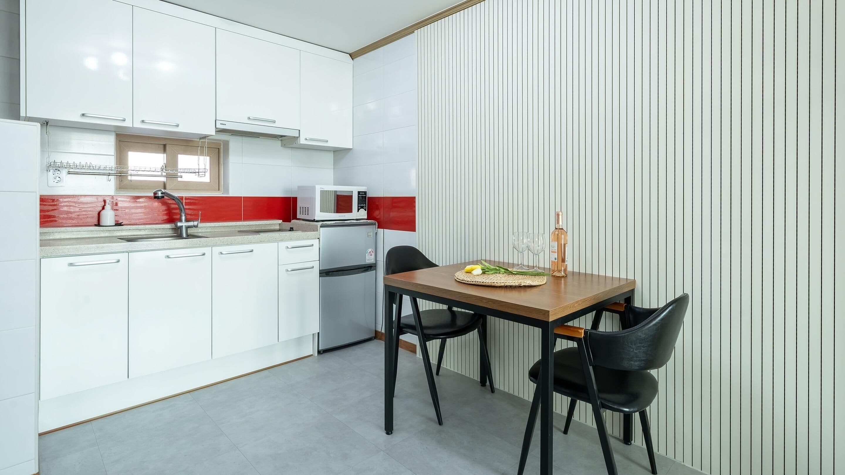 A modern kitchen with white cabinets, a red backsplash, and a dining area with a wooden table and black chairs.
