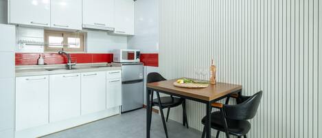 A modern kitchen with white cabinets, a red backsplash, and a dining area with a wooden table and black chairs.