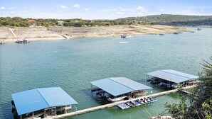 A waterfront property with multiple docked boats, a covered boat house, and a view of the surrounding landscape. - Luxury Waterfront Condo  Pool + Hot tub  Sleeps 4 (Spicewood)