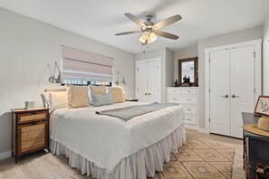 Um quarto com cama, ventoinha no teto, cómoda, guarda-roupa e mesa de cabeceira.