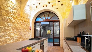 A kitchen with a stone wall, an arched doorway, and a countertop with vegetables. - Mixel Gozitan Villa and Pool (Sannat)