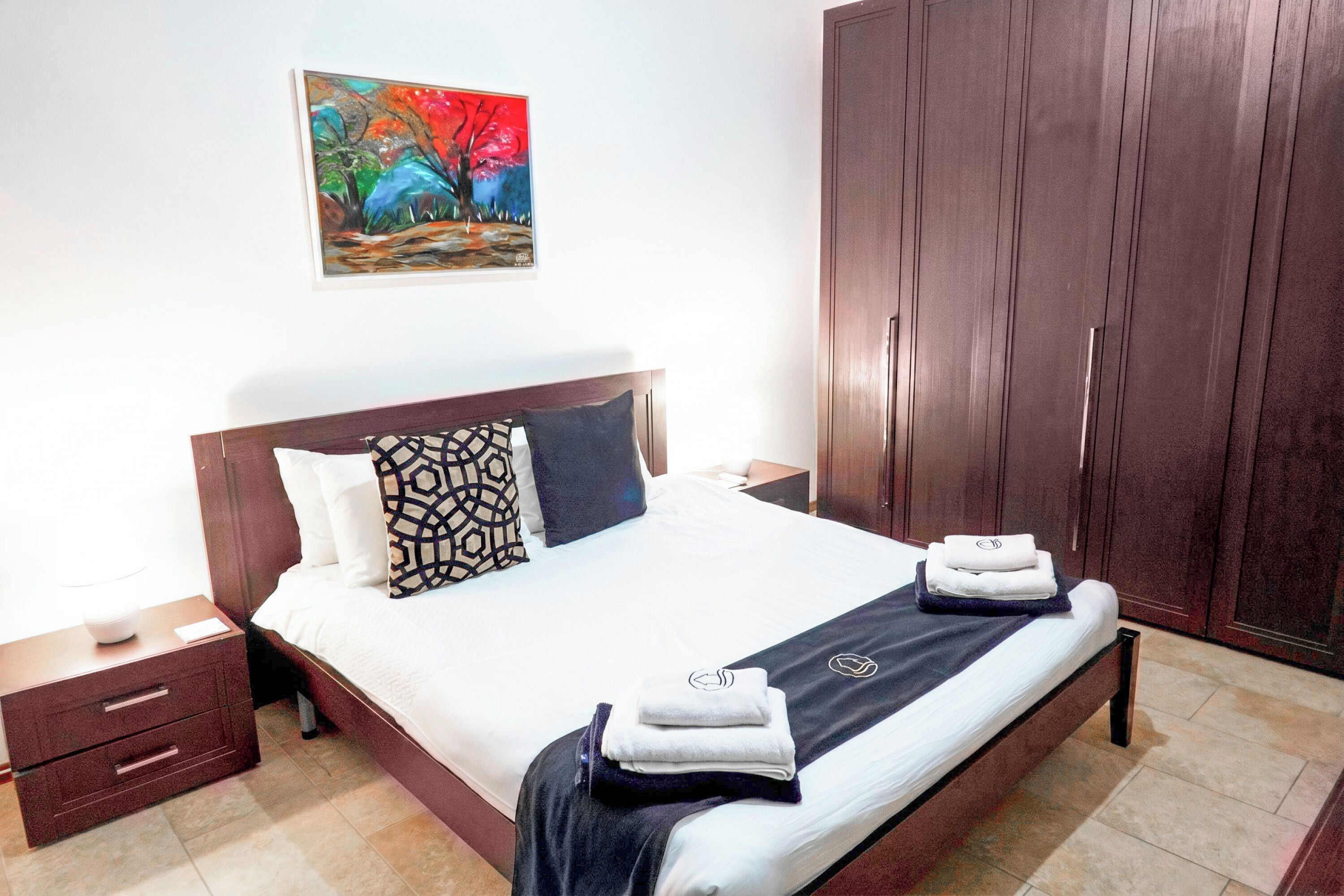 A neatly made bed with a patterned pillow, a bedside table with a lamp, and a large wardrobe.
