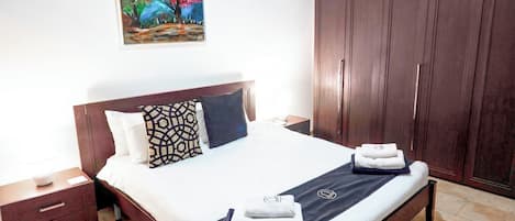 A neatly made bed with a patterned pillow, a bedside table with a lamp, and a large wardrobe.
