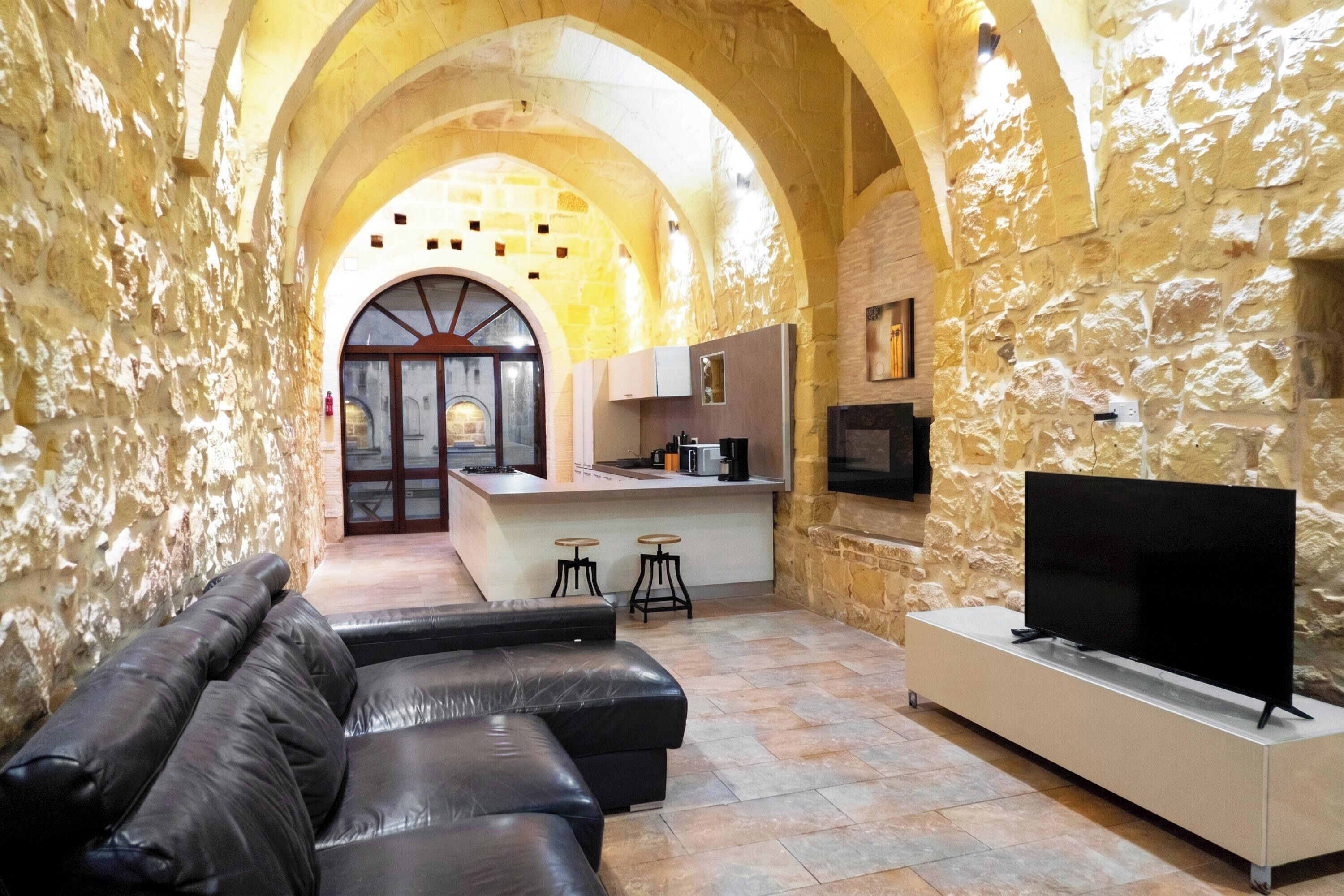 A stone-walled interior with a living area, a kitchen, and a TV.