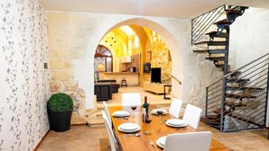 A dining area with a wooden table set for four, a stone wall, and a staircase. - Mixel Gozitan Villa and Pool (Sannat)