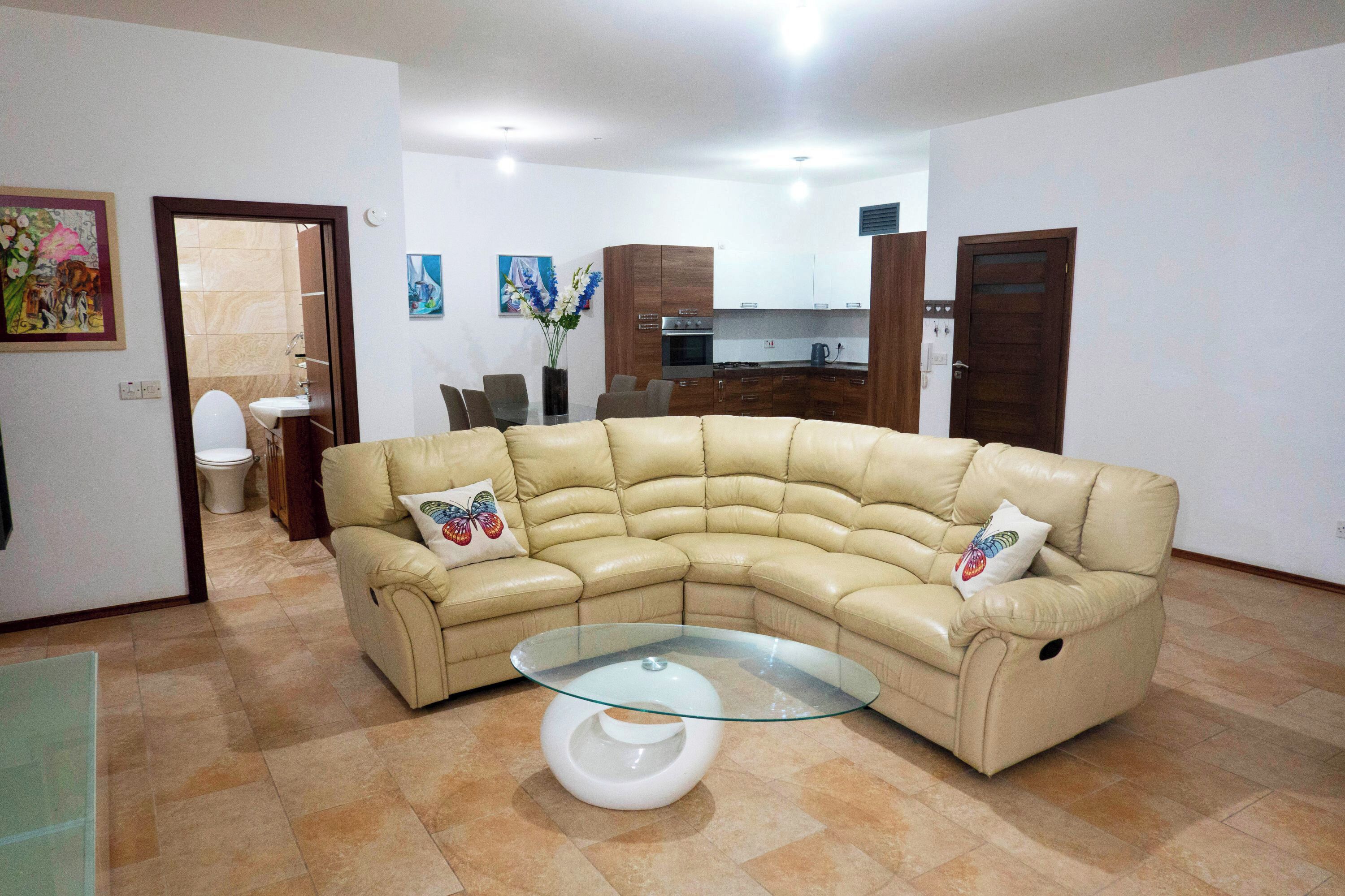 Ein Wohnzimmer mit einem beigefarbenen Ledersofa, einem Glastisch und einem Essbereich mit Stühlen.