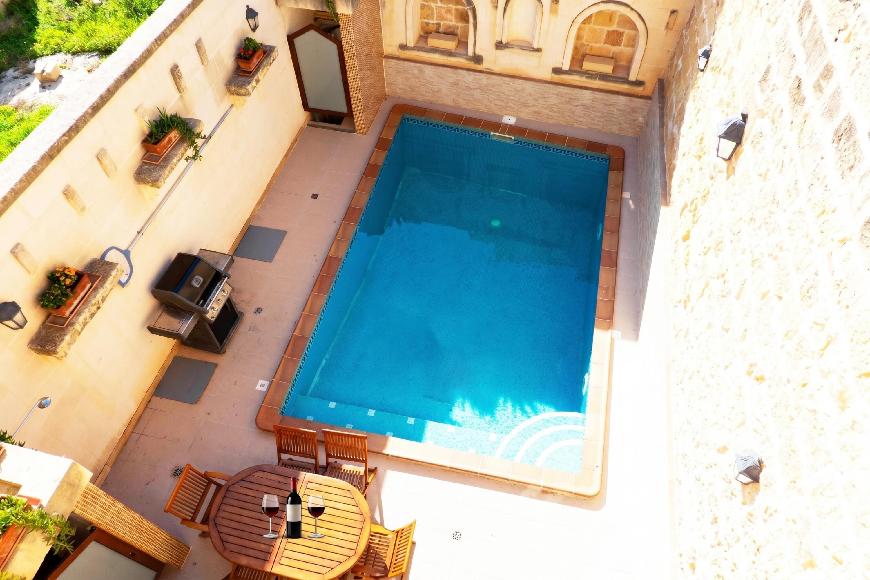 Piscina al aire libre con zona de barbacoa, asientos y plantas en macetas.