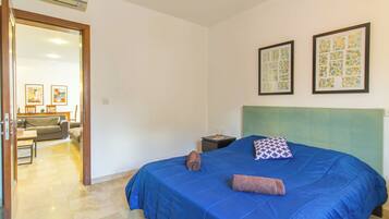A bedroom with a blue bedspread, a green headboard, and two framed artworks on the wall.