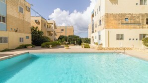 A swimming pool surrounded by buildings with balconies and a clear sky. - Seaview Pool Dolmen Apt St Paul's Bay (St. Paul's Bay)