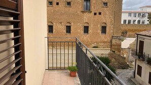 A balcony with a tiled floor, a potted plant, and a view of a historic building with multiple windows. - A La Batìa - Ospitalità Diffusa (Partanna)