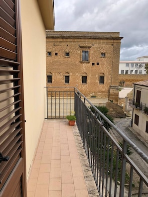 Varanda com piso de azulejos, vaso de planta e vista de um edifício histórico com várias janelas.