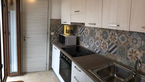 A kitchen with a microwave, oven, sink, and patterned backsplash. - A La Batìa - Ospitalità Diffusa (Partanna)