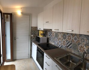 A kitchen with a microwave, oven, sink, and patterned backsplash.
