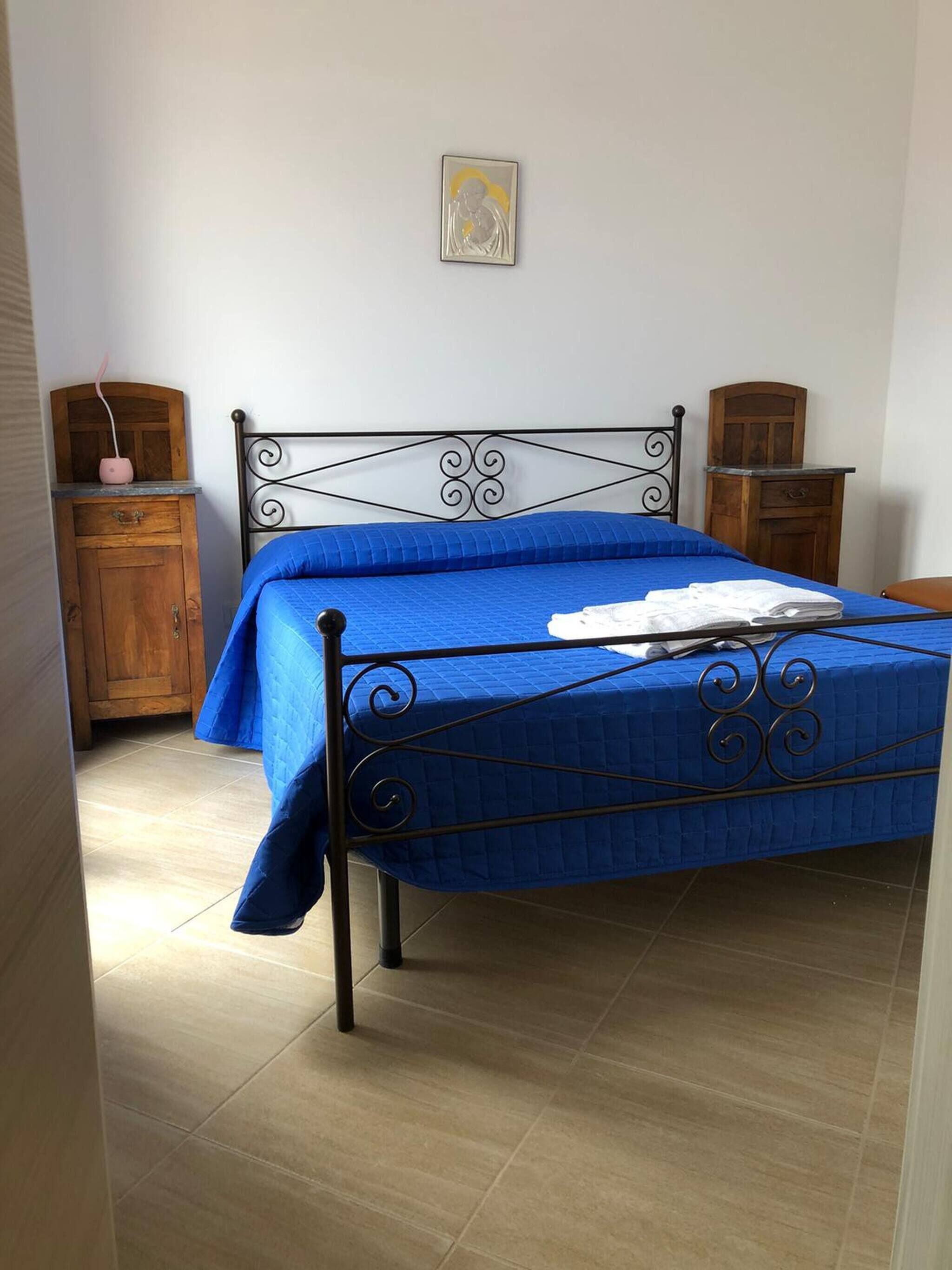 A bedroom with a metal bed frame, a blue bedspread, a wooden nightstand, a wooden dresser, and a wall-mounted picture.