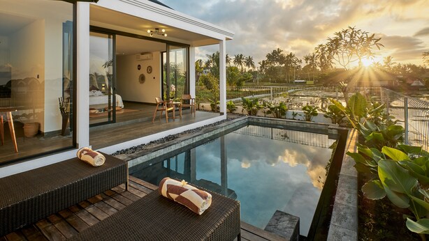Un área de piscina exterior moderna con un salón de cristal, terraza de madera y vistas del paisaje circundante.