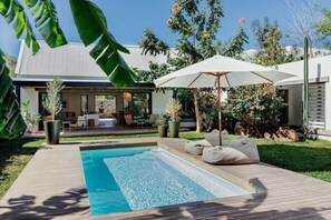 Een modern zwembad met terras, een ligstoel en een grote parasol.