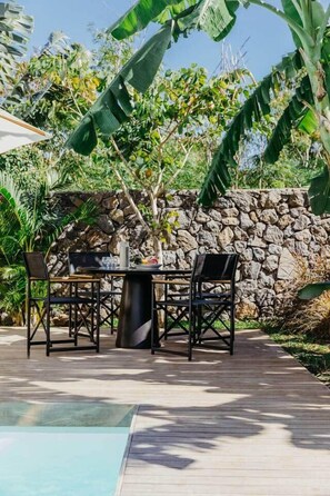An outdoor dining area with a stone wall, a pool, and tropical vegetation. - 3 bedroom villa nestled in nature (Black River Gorges)