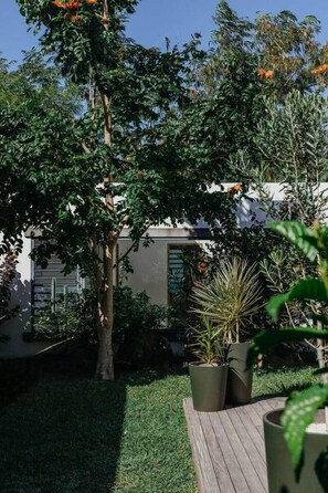 A garden with a wooden deck, potted plants, and a building in the background. - 3 bedroom villa nestled in nature (Black River Gorges)