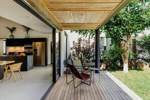 Een moderne keuken met een inbouw eiland, een eetgedeelte met een houten terras, en uitzicht op een tuin met bomen en rotsen.