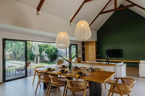 Un espace repas avec une grande table, des chaises en osier et des luminaires suspendus.