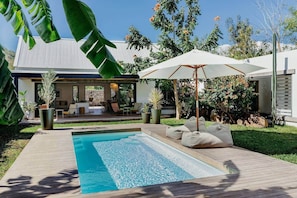 Een modern zwembad met terras, een ligstoel en een grote parasol.