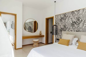 Een slaapkamer met een bed, een ronde spiegel, een nachtkastje, een klein krukje, een hangende lamp en een behang met een patroon.