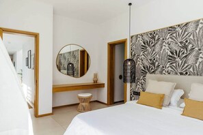 Une chambre à coucher avec un lit, un miroir rond, une table de chevet, un petit tabouret, un luminaire suspendu et un mur à motifs.