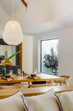 Een eethoek met een groot raam, een hanglamp en een plant op tafel.