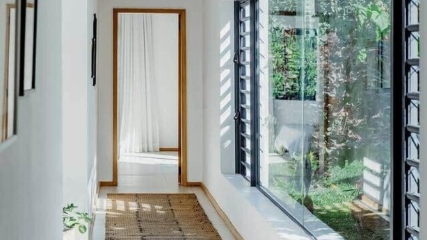 Un couloir étroit, avec une grande fenêtre d’un côté, une porte au fond et un tapis tissé sur le sol.