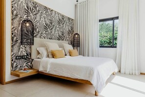 Een moderne slaapkamer met een bed, witte beddengoed, een behang met patroon, en een raam met gordijnen.