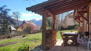 A covered patio with a table and chairs, a grill, and a view of mountains in the background.