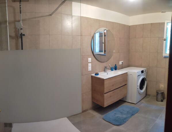 Un baño moderno con cabina de ducha de vidrio, un mueble de tocador de madera con lavadora integrada y un espejo redondo.