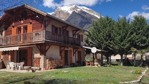 A chalet with a balcony, stone walls, and a mountain backdrop.