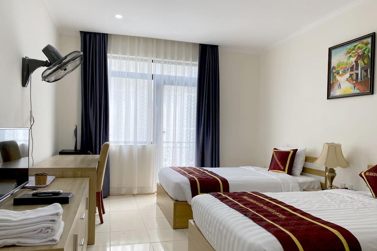 A hotel room with two beds, a desk with a chair, a lamp, and a painting on the wall.
