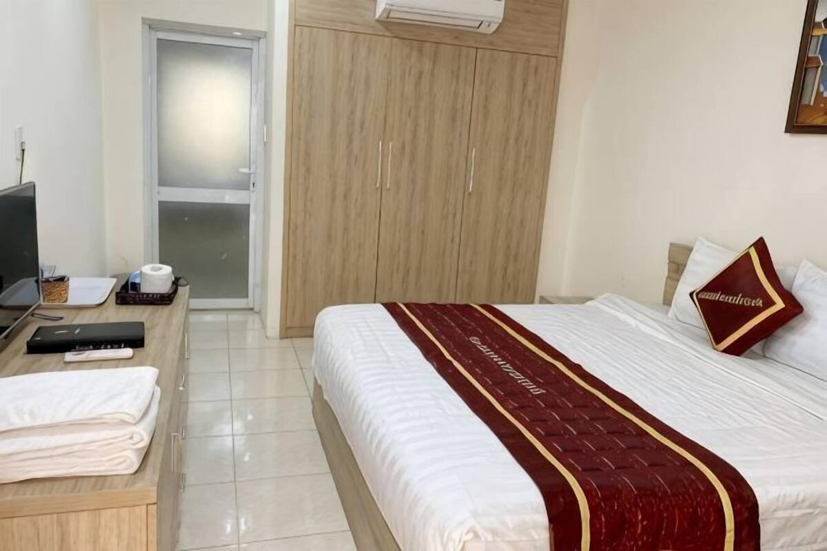 A hotel room with a bed, a desk with a computer, a television, and a wardrobe.