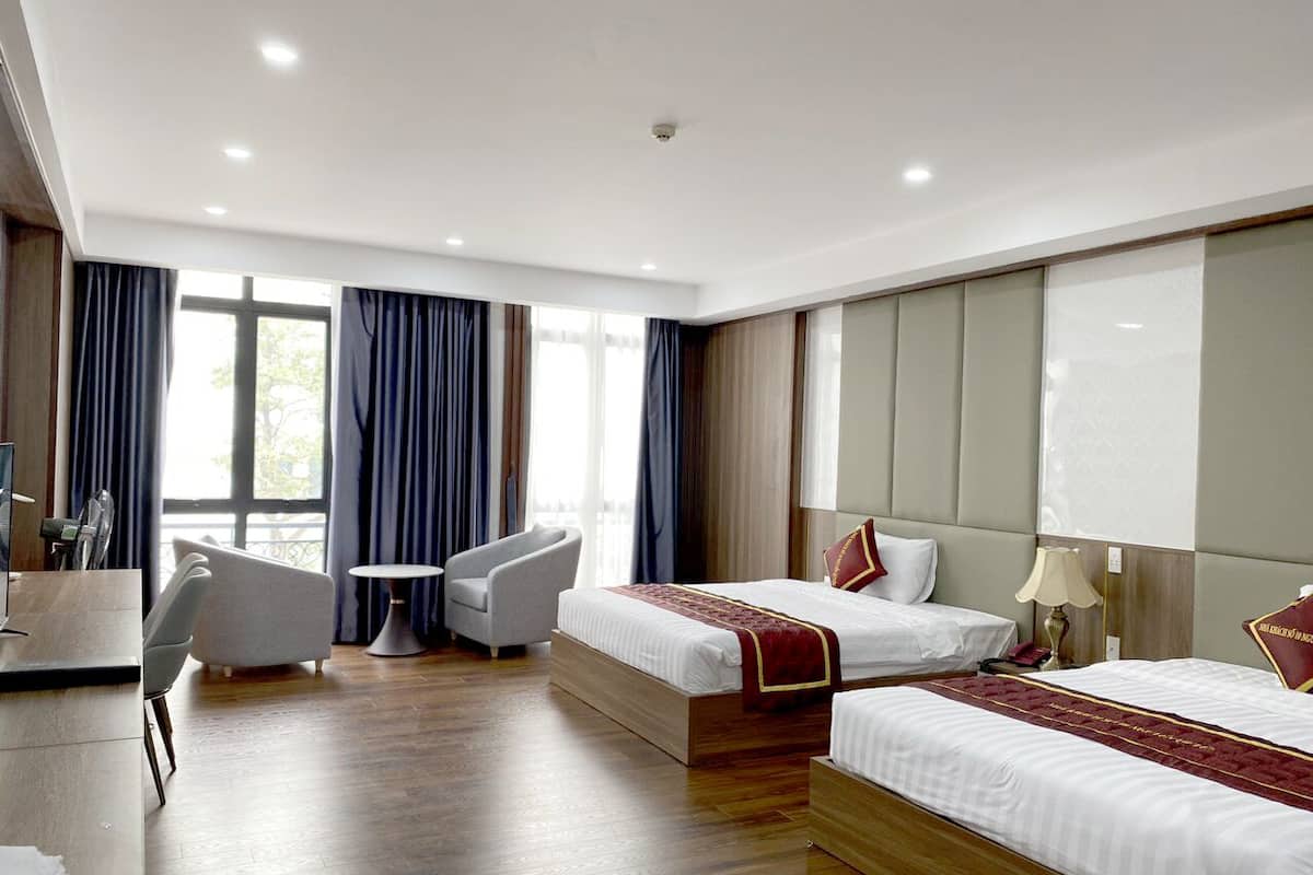 A hotel room with two beds, a desk, a chair, and a view of the outdoors.