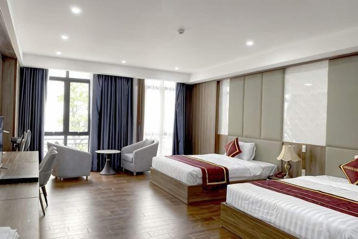 A hotel room with two beds, a desk, a chair, and a small table.