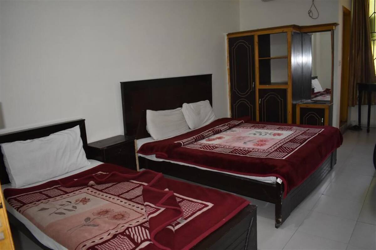 Two single beds with dark wooden headboards and white pillows, a red and beige patterned bedspread, and a wooden wardrobe with mirrored doors.
