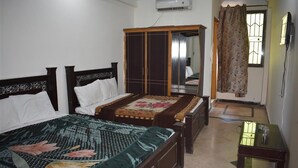 A bedroom with two single beds, a wardrobe, a small table, and a window with curtains. - Mehran Hotel (Rawalpindi)