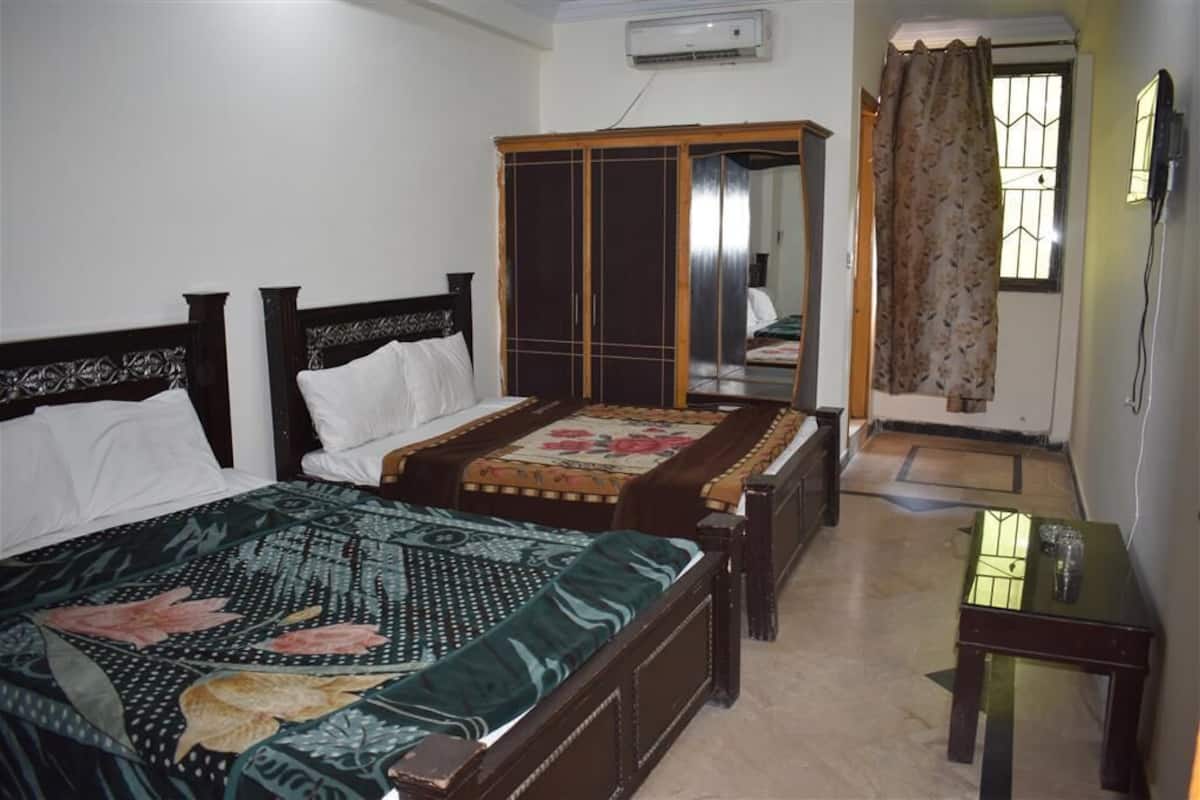 A bedroom with two single beds, a wardrobe, a small table, and a window with curtains.
