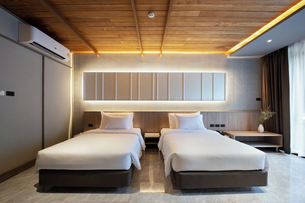 Habitación de hotel moderna con dos camas, techo de madera, un panel grande montado en la pared y una mesita de noche con un florero.
