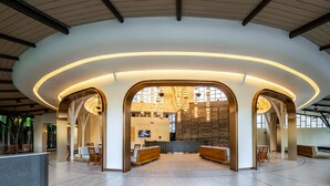 A spacious lobby with a curved ceiling, wooden reception desk, seating areas, and a large wall with a TV screen. - Luminous Resort & Spa by Areca (Kathu)