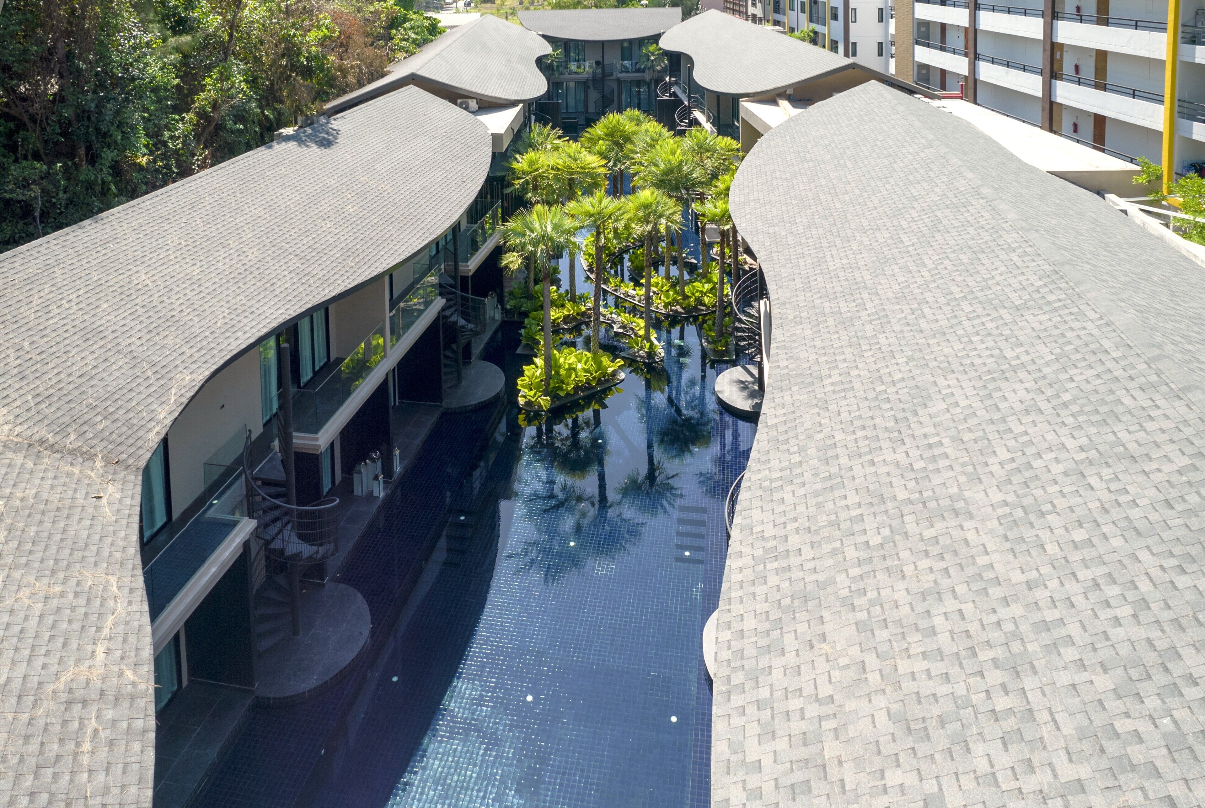 A modern hotel with a central swimming pool surrounded by lush greenery and a multi-level building with balconies.
