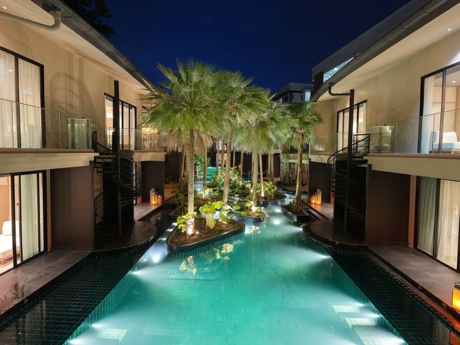 A modern hotel with a central swimming pool, surrounded by palm trees and illuminated by ambient lighting.