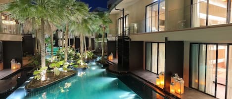 A swimming pool with a glass barrier, surrounded by palm trees and indoor lighting.