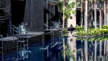 Piscina con escalones de cerámica y fuente de agua, rodeada de palmeras y vegetación.