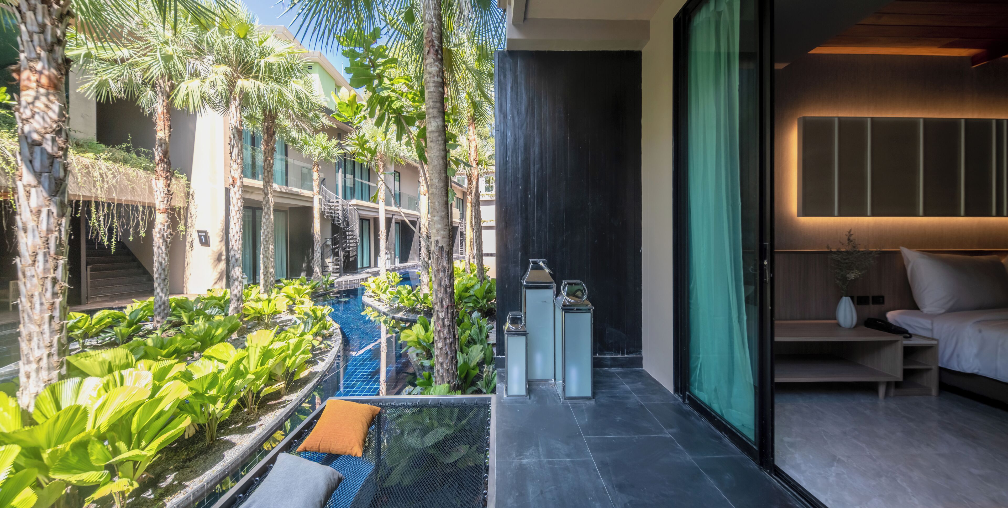 A modern hotel room with a balcony overlooking a pool and lush greenery.